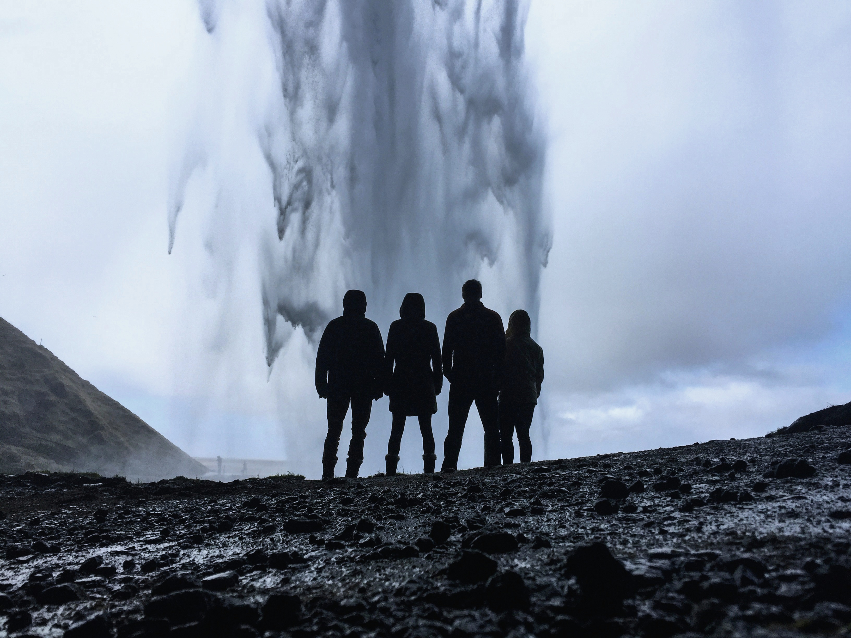 Die Silhouetten von fünf Personen vor einem Geysir auf Lavagestein