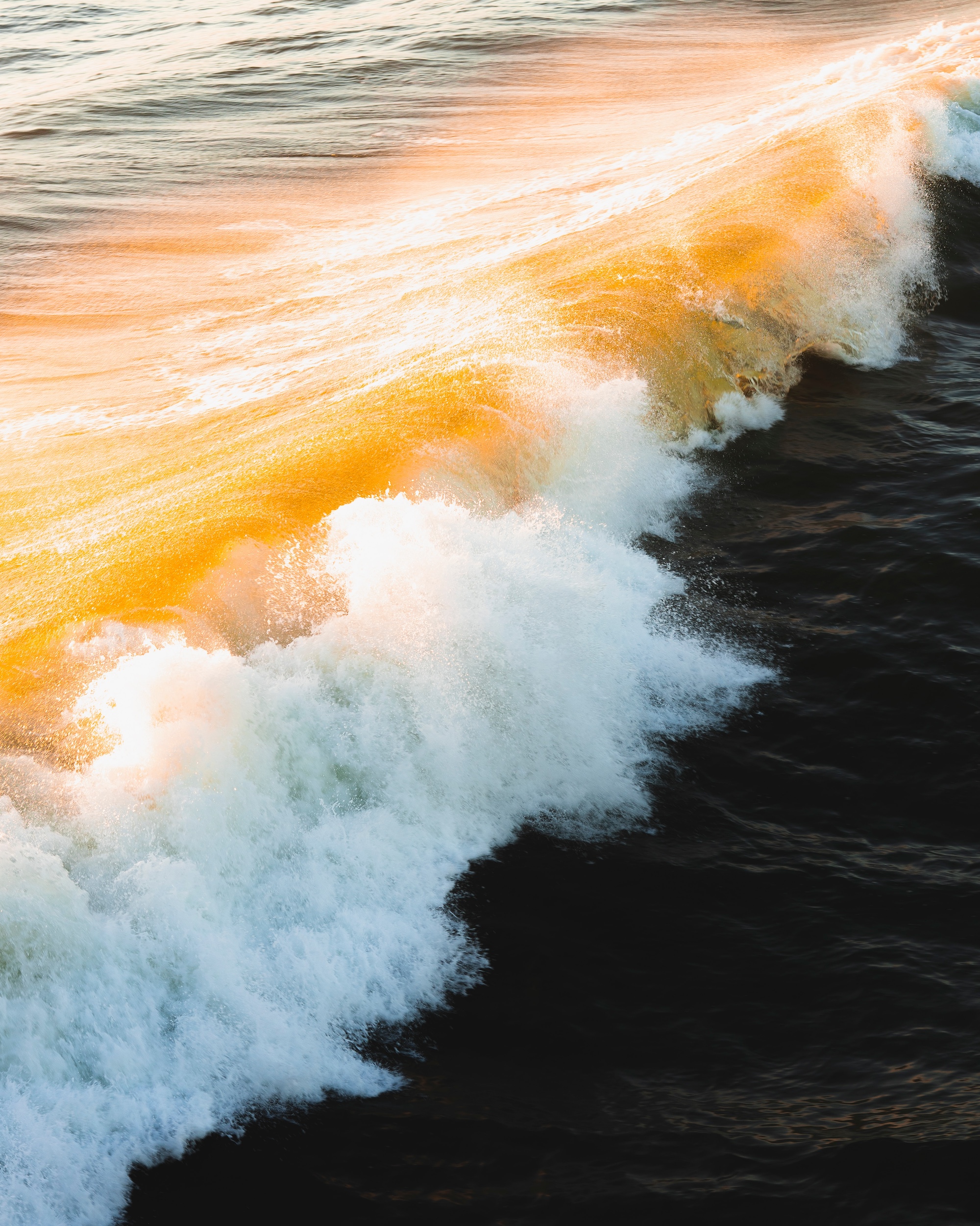 Orange durchleuchtete Welle in dunklem Wasser